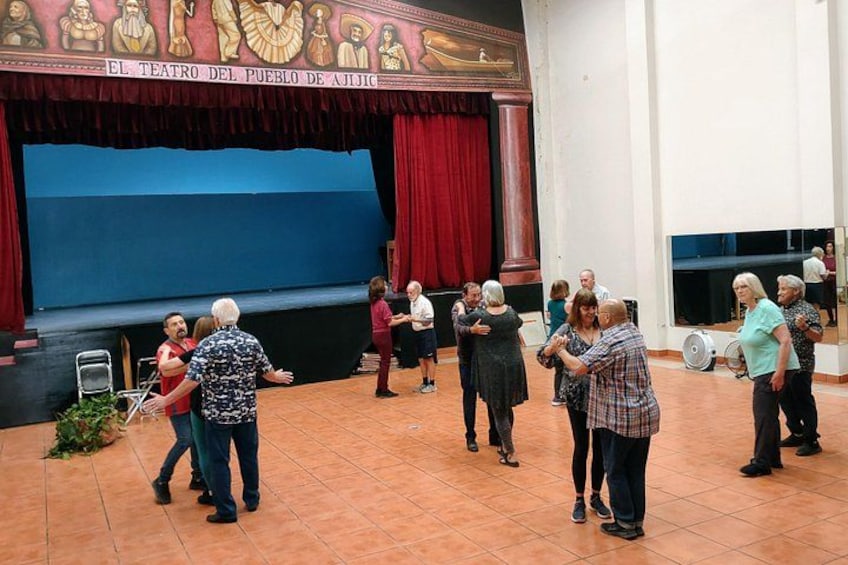 En grupp människor som dansar i en teater med en scen och röda draperier. 2