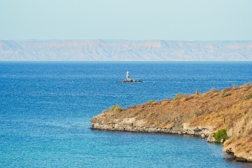 Un paysage côtier avec un phare situé sur une petite île, une mer bleue et limpide, et des falaises rocheuses. 1