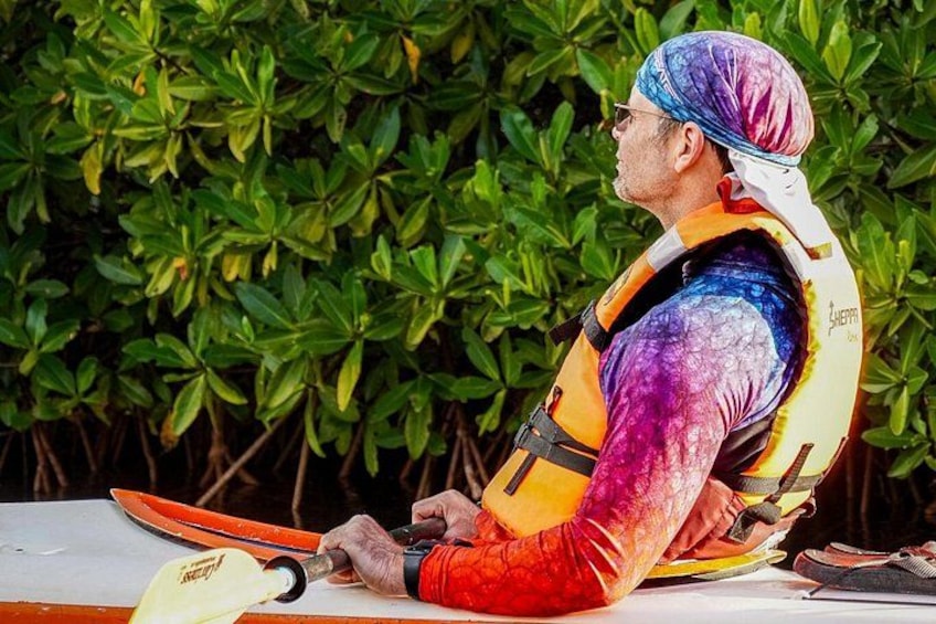 A person sitting outdoors with a kayak, wearing a life jacket and a colorful shirt. 5