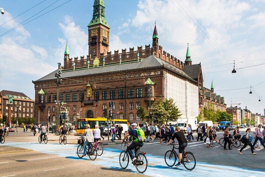En travl gade med cyklister og en historisk bygning med et tårn og et ur. 2