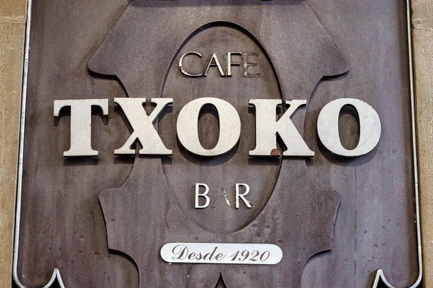 Een metalen bord met de tekst 'CAFE TXOKO BR' en 'Desde 1920', dat de naam en het oprichtingsjaar van het café aangeeft. 2