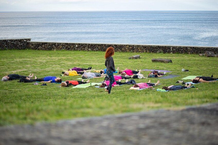 A group of people lying on the grass in a circle, facing the ocean. 2