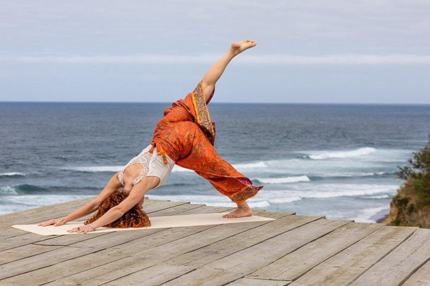 A person performing a yoga pose on a wooden deck by the ocean. 3