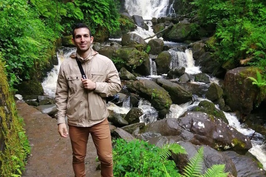 Una persona parada en un sendero con una cascada al fondo. 2