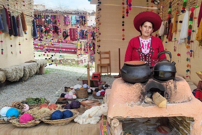 A person in traditional attire with a large pot and a kettle on a stove, surrounded by colorful textiles and baskets. 2