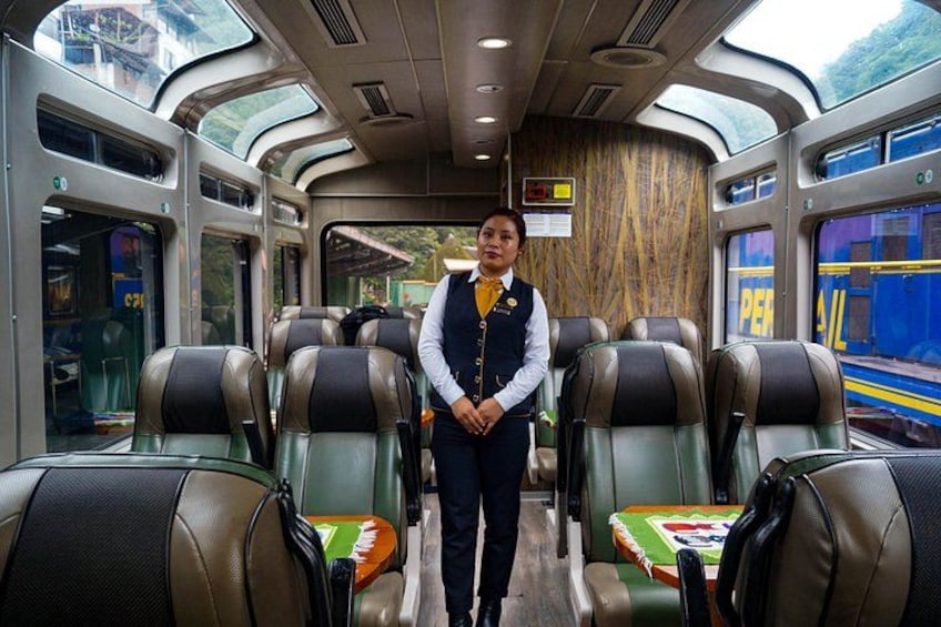A train interior with a conductor standing, rows of seats, and a wooden wall. 1