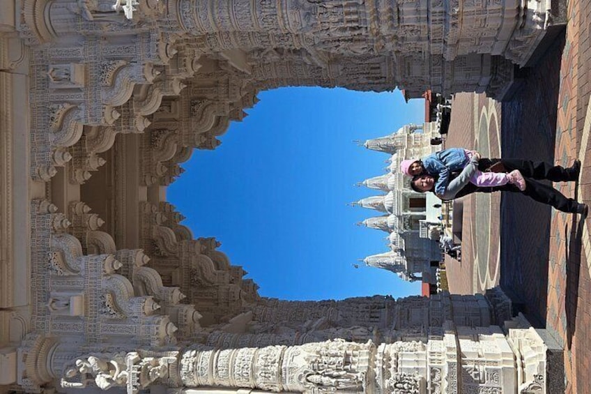 A person standing in front of a large, ornate architectural structure with intricate carvings and a clear blue sky in the background. 2