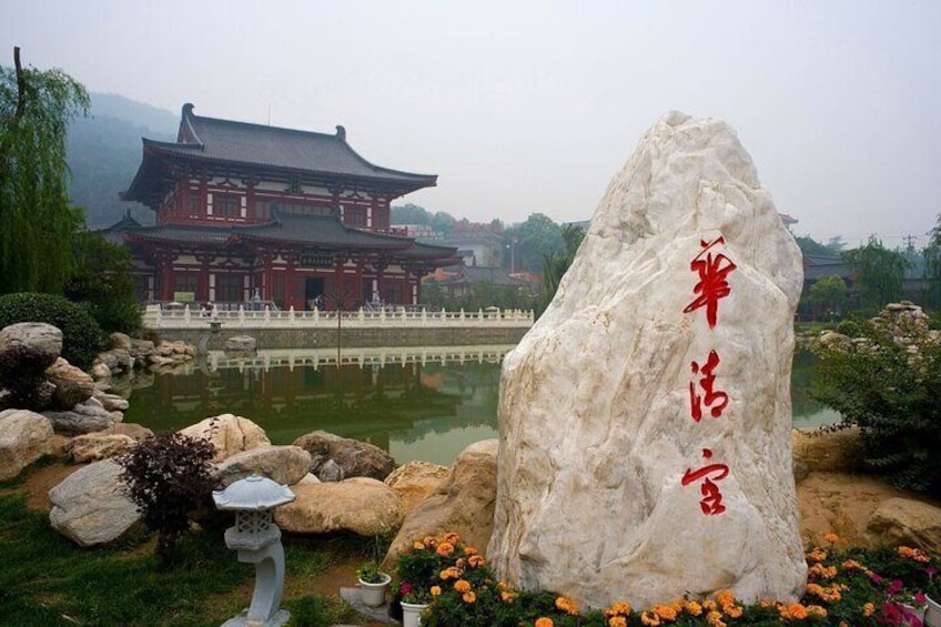 A traditional building with a large rock inscribed with red characters, a pond, and a stone lantern. 1