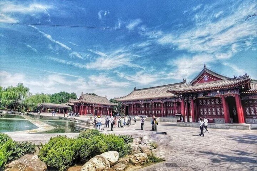 A traditional Chinese building with red walls and a tiled roof, surrounded by a stone courtyard and a small pond. 1