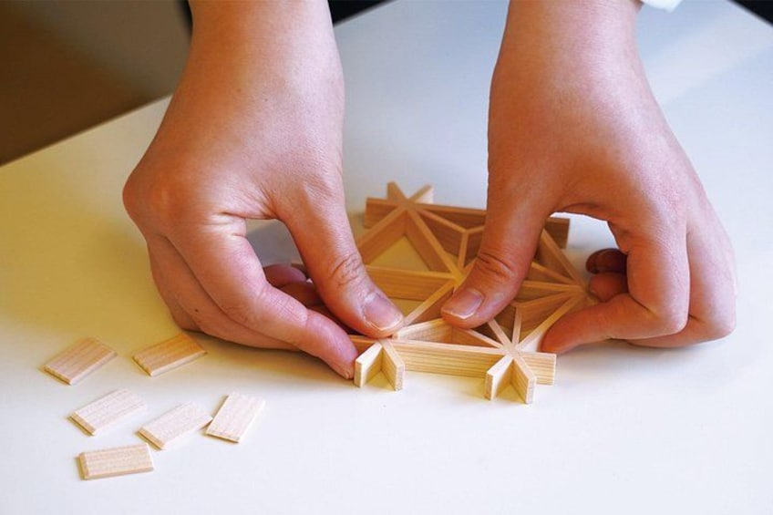 Hände setzen Holz-Geometrieformen auf einer weißen Unterlage zusammen. 1