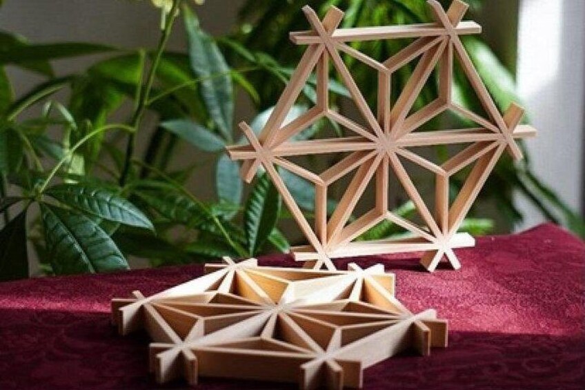 Eine geometrische Holzskulptur auf einer roten Stoffoberfläche, im Hintergrund grünes Laub. 3