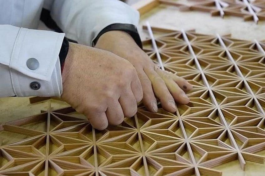 Hände arbeiten an einem geometrischen Muster aus Holz. 4