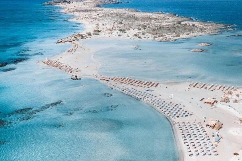 An aerial view of a beach with clear blue waters, a sandy shore, and rows of beach umbrellas. 2