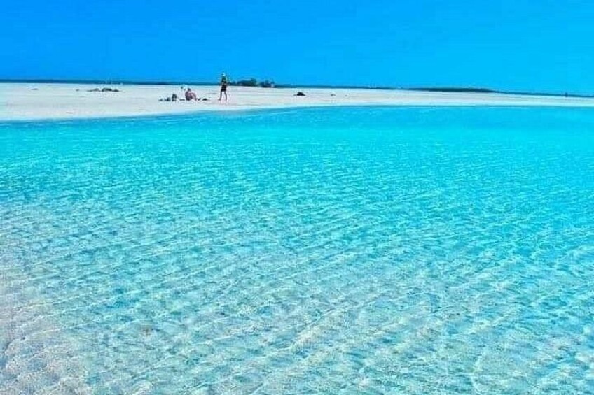 A beach with clear turquoise water and a person walking on the sand. 5