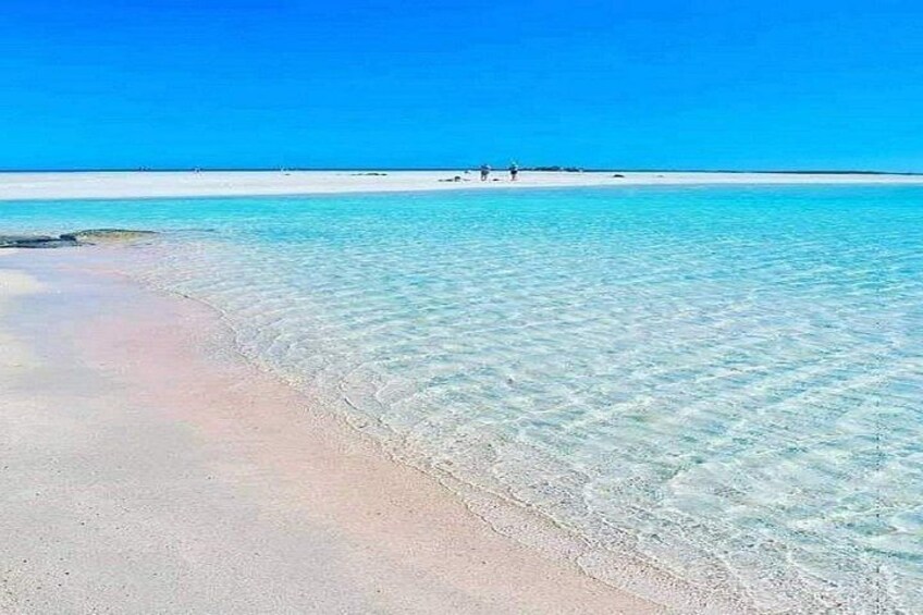 A beach with clear turquoise water, a sandy shore, and a small island in the distance. 3