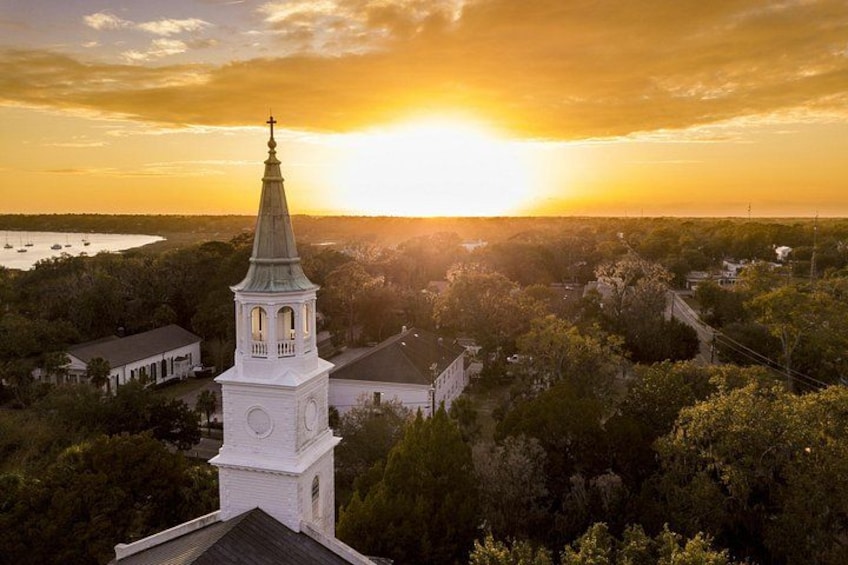 A church with a steeple, surrounded by trees and buildings, during sunset. 2