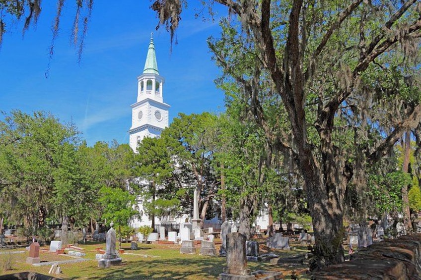 A cemetery with a church tower, gravestones, and trees. 1