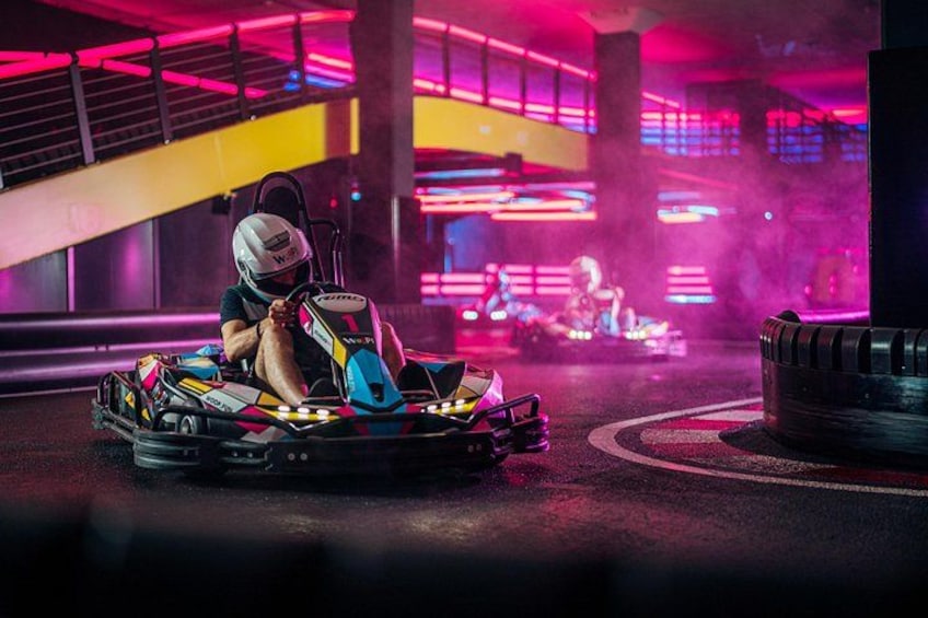 A go-kart track with a go-kart and driver in the foreground. 1