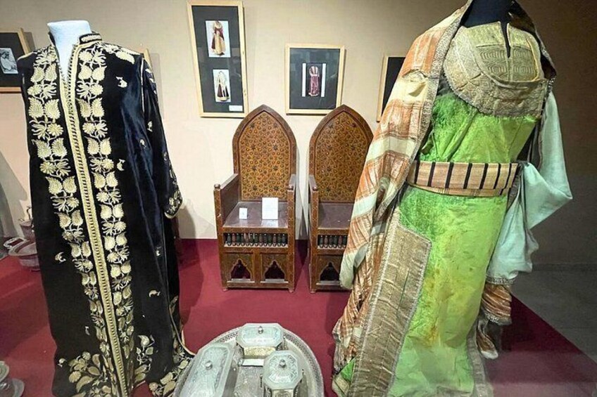 Mannequins dressed in historical garments, a wooden chair, and a decorative metal object. 4