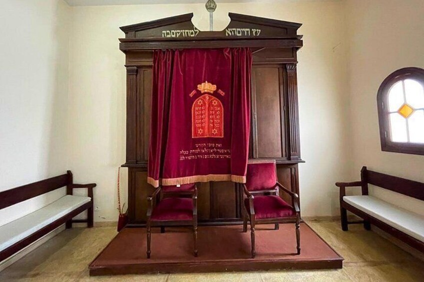A wooden structure with two chairs, a red cloth, and Hebrew inscriptions. 5