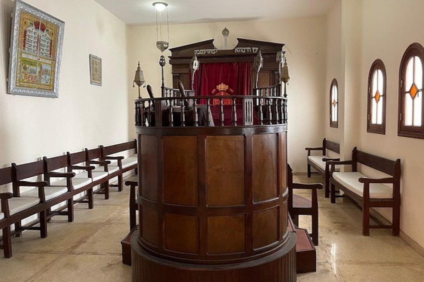 A wooden pulpit with a red curtain, wooden benches, and arched windows. 4