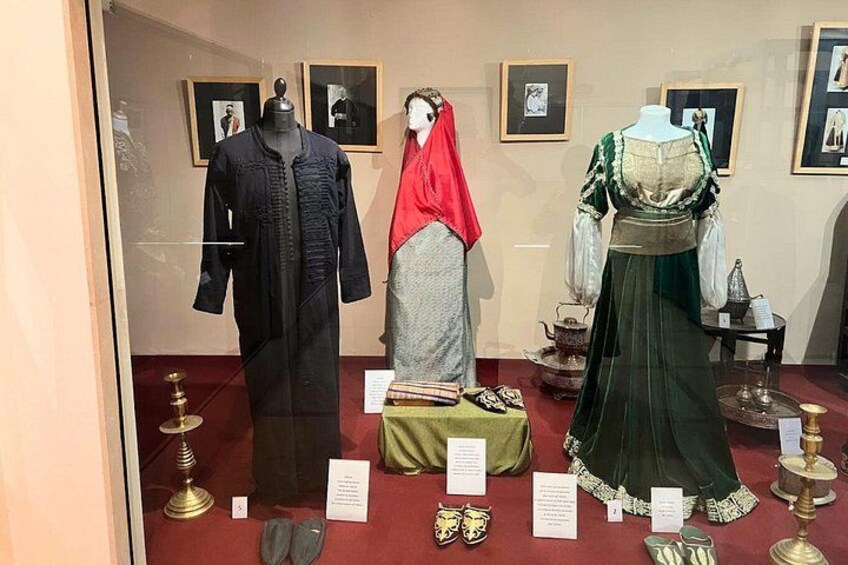 Mannequins dressed in historical clothing, with a red shawl and a green dress, displayed in a museum setting with informational placards. 3
