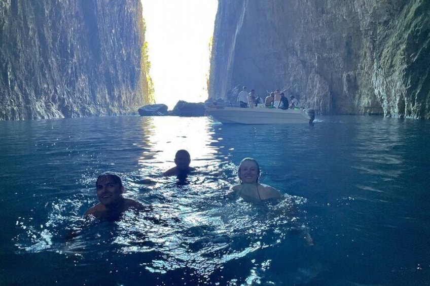 People swimming in a natural water body with a rocky cave in the background. 1