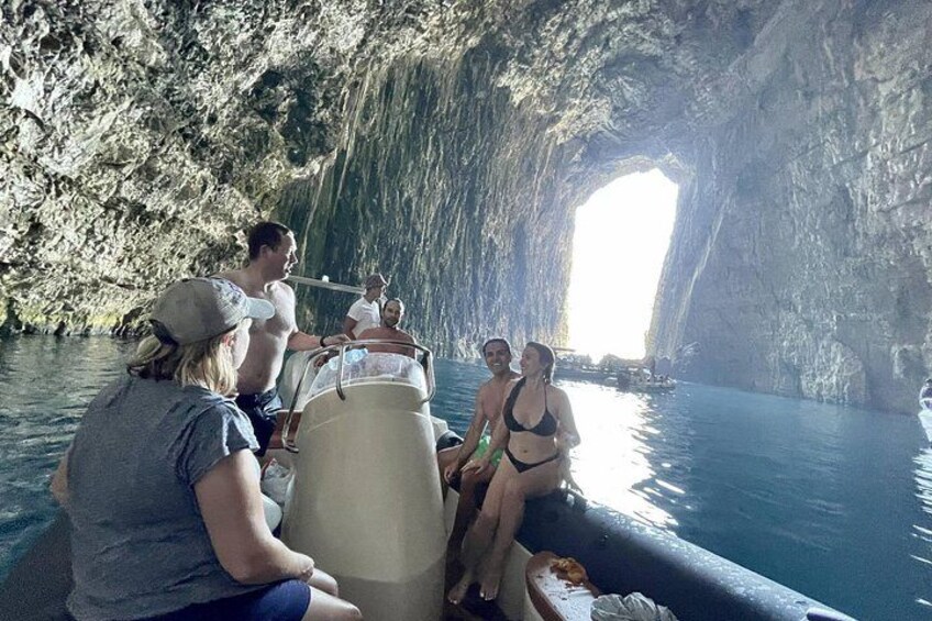 A group of people on a boat near a large cave opening. 3