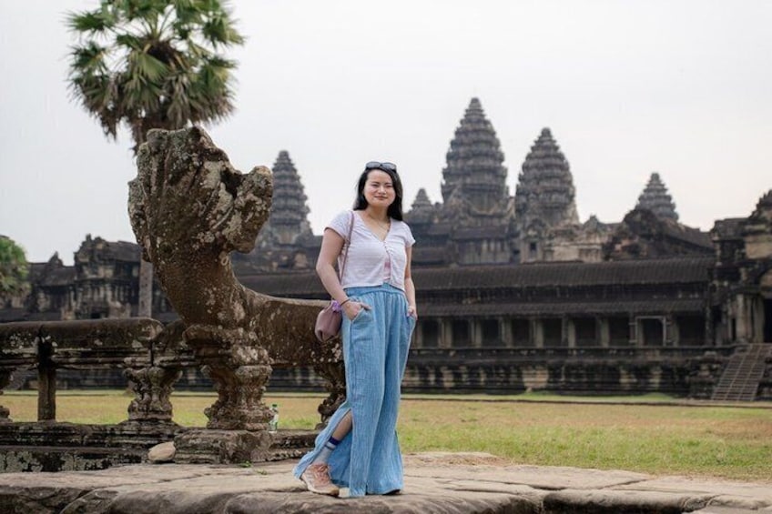Una persona de pie frente al templo de Angkor Wat, con un león de piedra y arquitectura antigua al fondo. 2