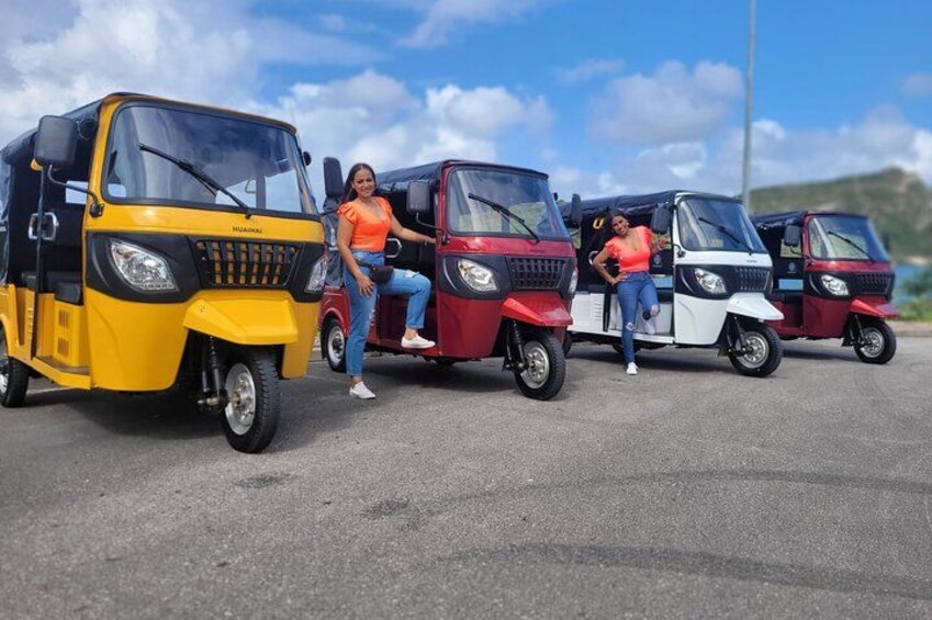 Tres tuk-tuks estacionados en una calle, con dos personas de pie junto a ellos. 1