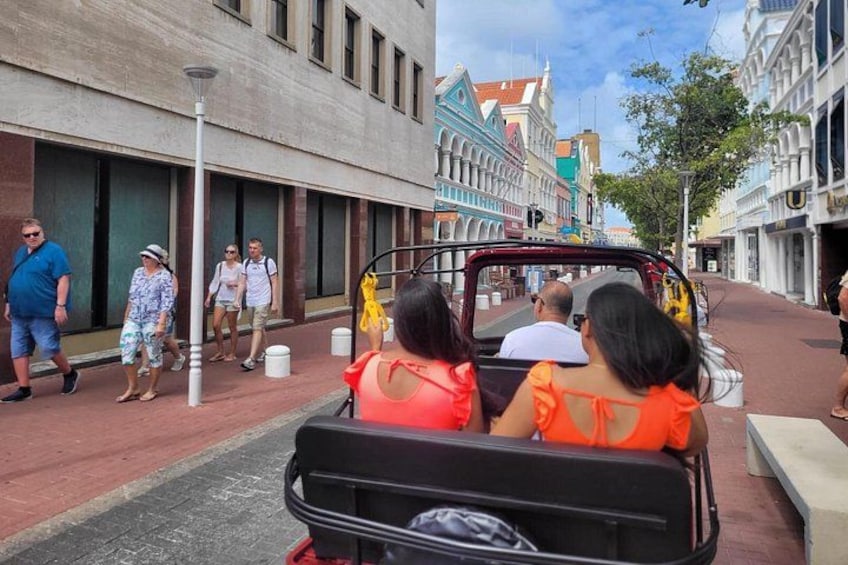 A street with a vehicle carrying passengers, buildings, and pedestrians. 4