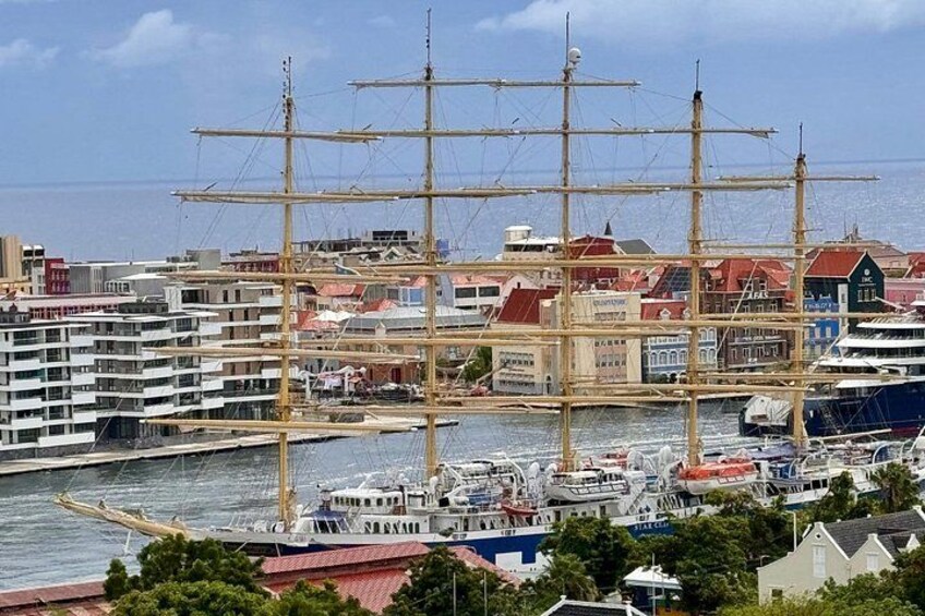 A large sailing ship docked in a harbor with modern buildings and boats in the background. 3