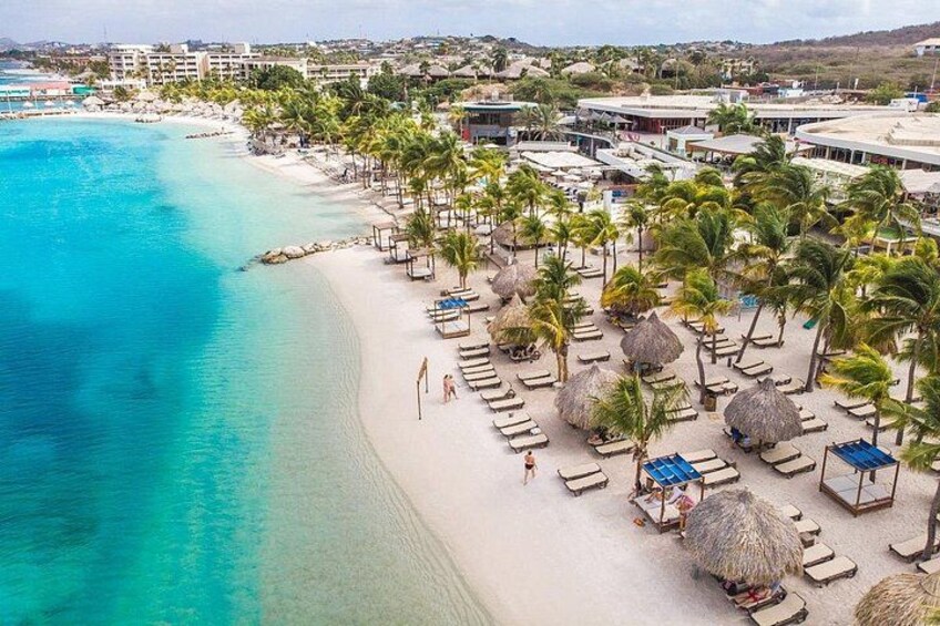 Una playa con agua turquesa cristalina, palmeras y sombrillas. 2