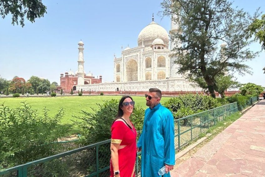 Una coppia in piedi di fronte al Taj Mahal, con un giardino e una recinzione sullo sfondo. 2