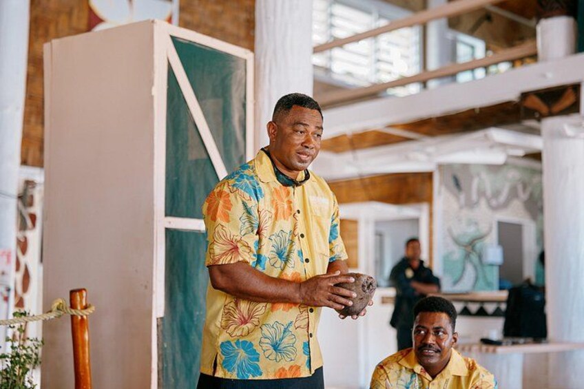 A person in a yellow shirt with a floral pattern, standing indoors with a large white cabinet and a glass door in the background. 2