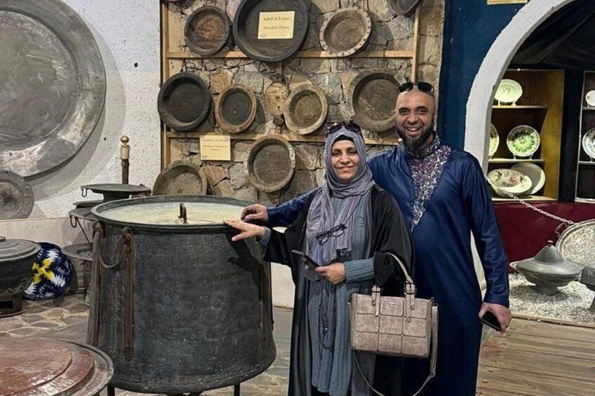 A person standing next to a large metal container, with various plates and bowls displayed on the wall behind. 3
