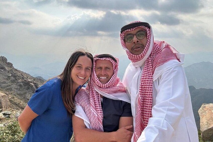 Three people standing on a rocky outcrop with a mountainous landscape in the background. 4