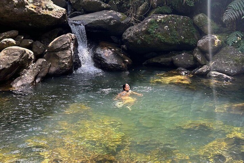 Une personne nage dans une étendue d’eau claire, entourée de rochers et d’une cascade. 1