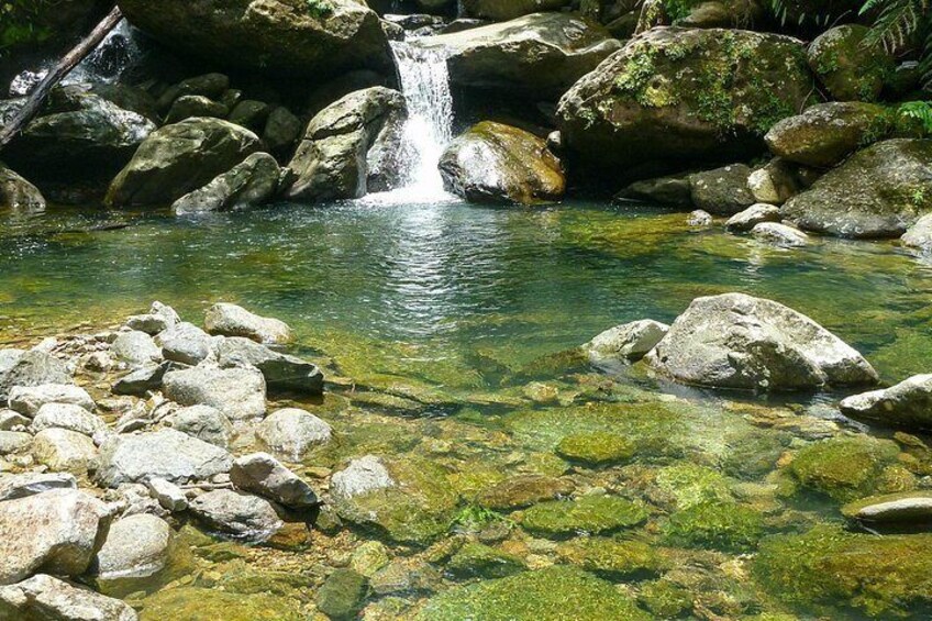 Un ruisseau aux eaux claires, parsemé de rochers, une cascade et une zone boisée. 2
