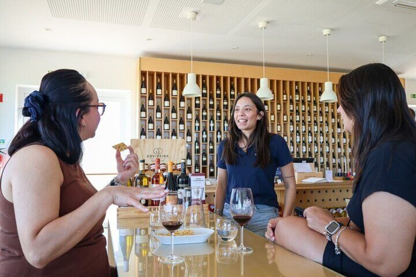 Drei Frauen probieren Wein an einer Bar, im Hintergrund eine Weinschlange. 1