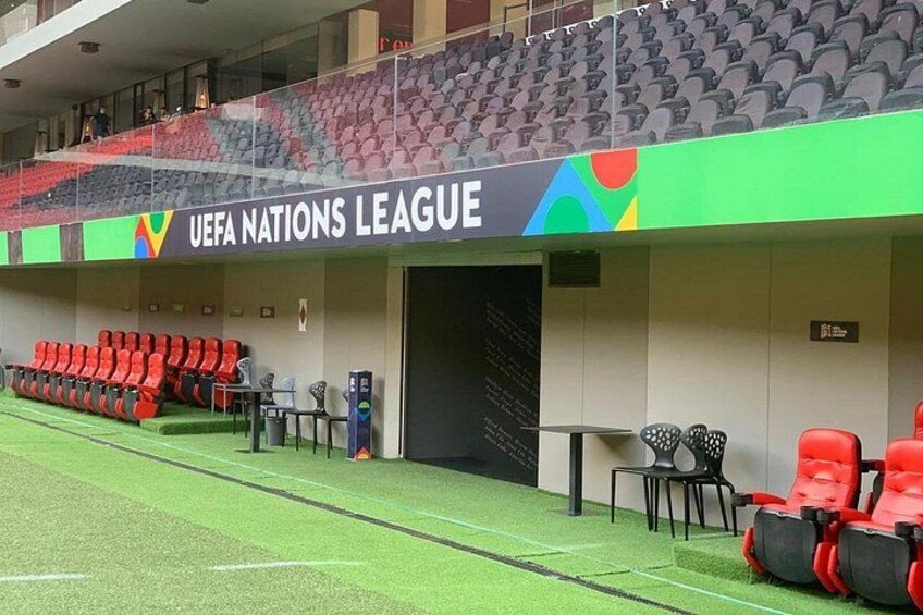 Un estadio con señalización de la Liga de Naciones de la UEFA, zonas de asientos y un campo de césped artificial verde. 1