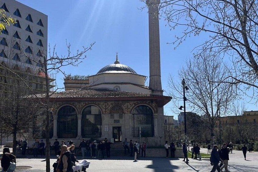 Un edificio histórico con una cúpula y una columna alta, rodeado de árboles y personas. 4