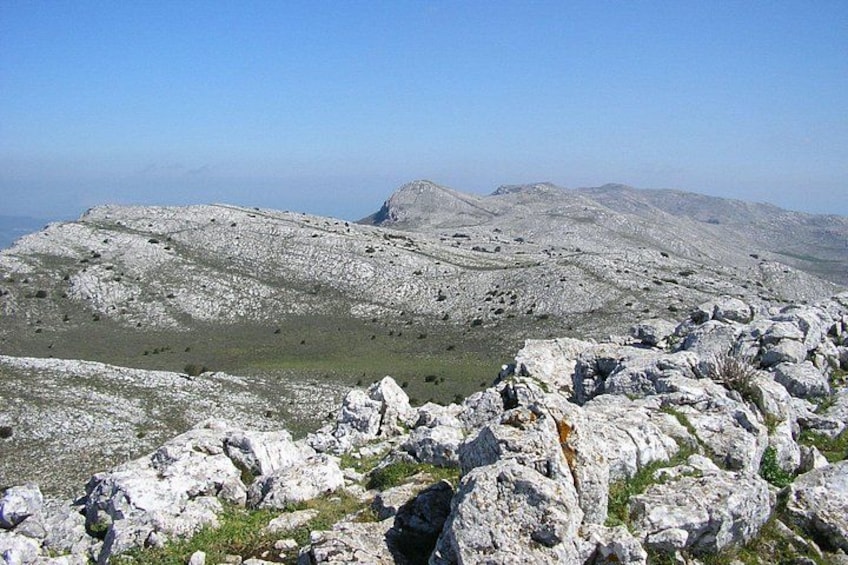 A rocky mountain landscape with sparse vegetation and distant hills. 3