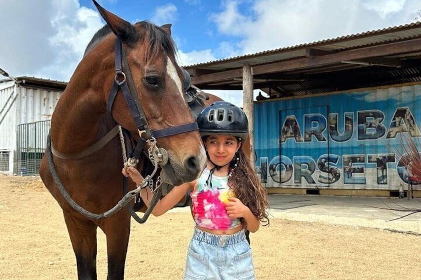 Ein Kind mit einem Pferd in einem Stallbereich, ein Schild mit der Aufschrift 'ARUBA HORSETO'. 3
