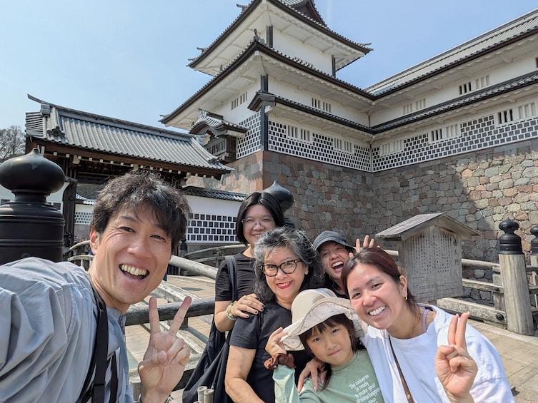 A group of people posing in front of a traditional Japanese building with a tiled roof and stone walls. 3