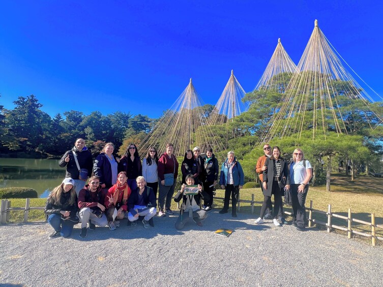 A group of people posing in front of traditional Japanese structures with a lake in the background. 1