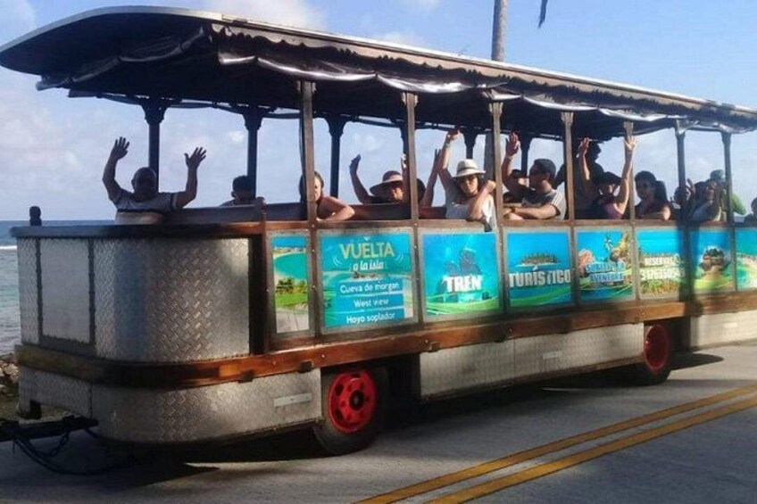 A bus with advertisements for tours, passengers raising their hands, and a coastal road. 5