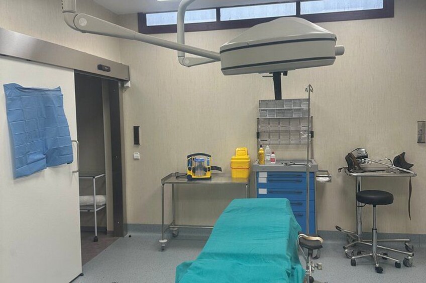 A medical examination room with a bed, examination table, medical equipment, and a window. 3