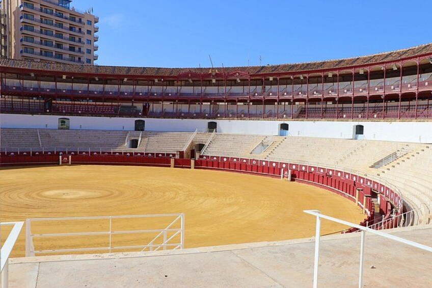 Una plaza de toros vacía con suelo de arena y asientos rojos. 5