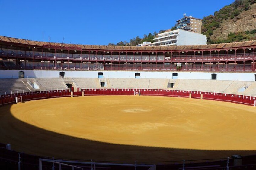 A bullring with a sandy arena, tiered seating, and a building in the background. 5